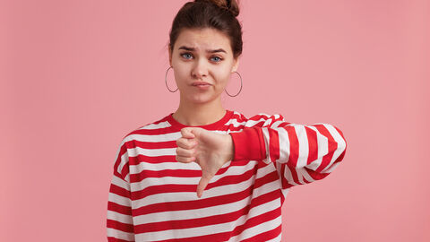 Beschwerde Button Junge Frau die mit einer Hand den Daumen der linken Hand nach unten streckt und dabei unerfreut schaut