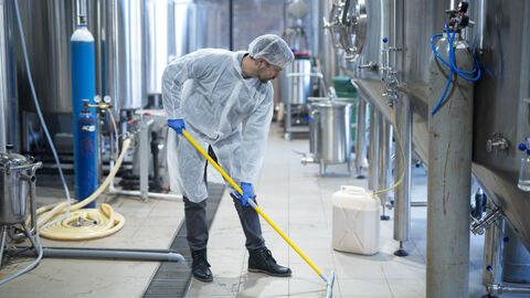 Hygienemängelmelder In einem Lebensmittel-Industriebetrieb wird der Boden von einer Person gewischt.